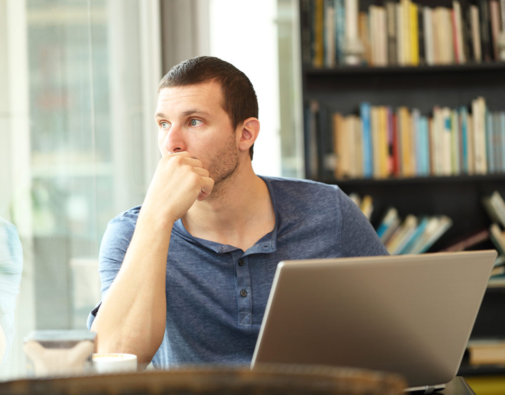 Pensive man using laptop looks through a window in a bar