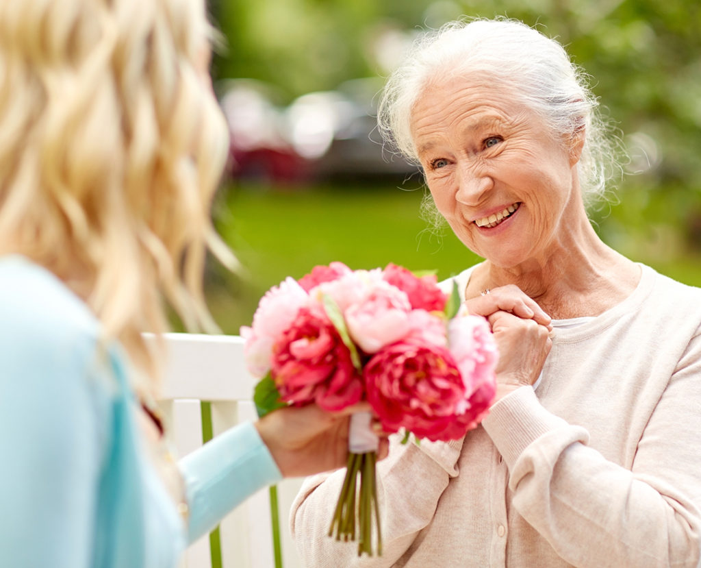 daughter giving flowers to senior mother at park