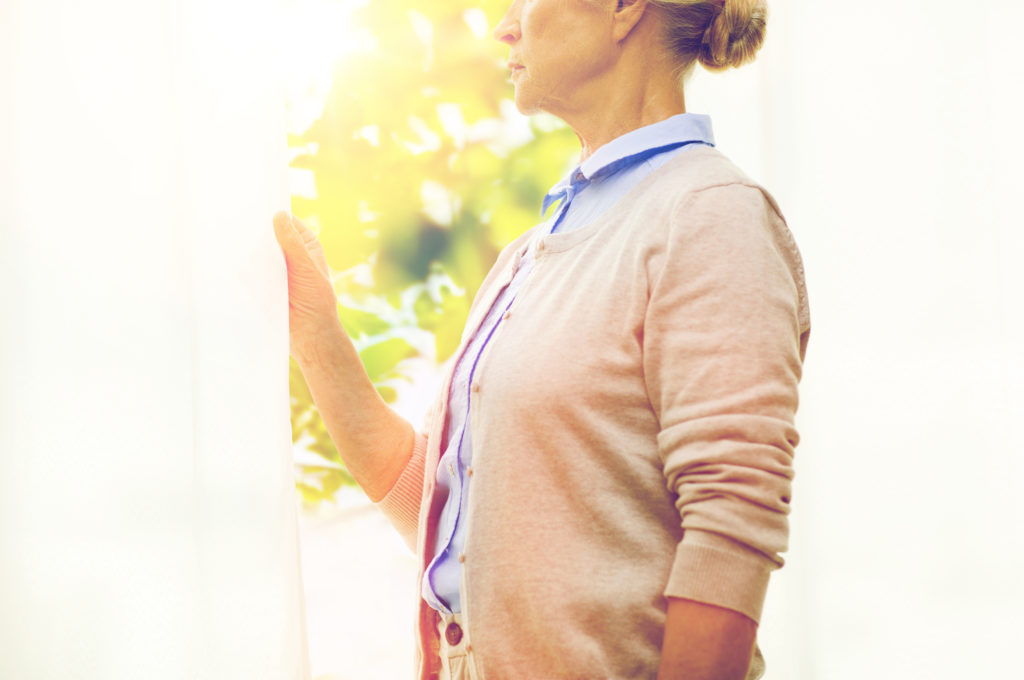 lonely senior woman looking through window at home