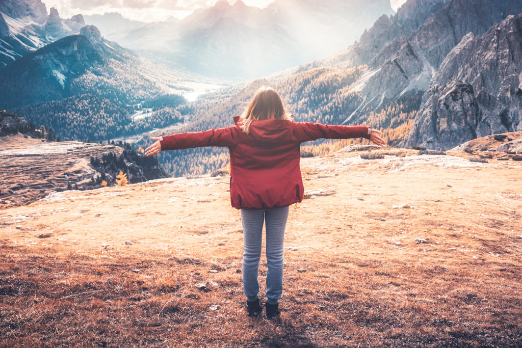 Young woman with raised up arms and mountains at sunset