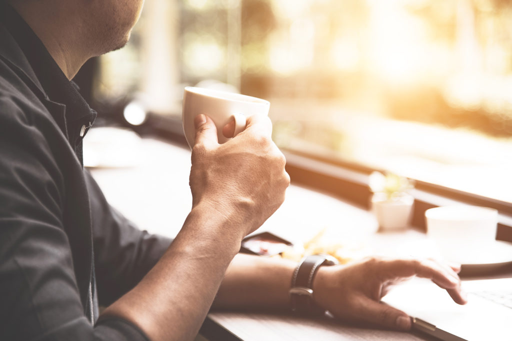 Close up of coffee cup on businessman hand. Man working with lap