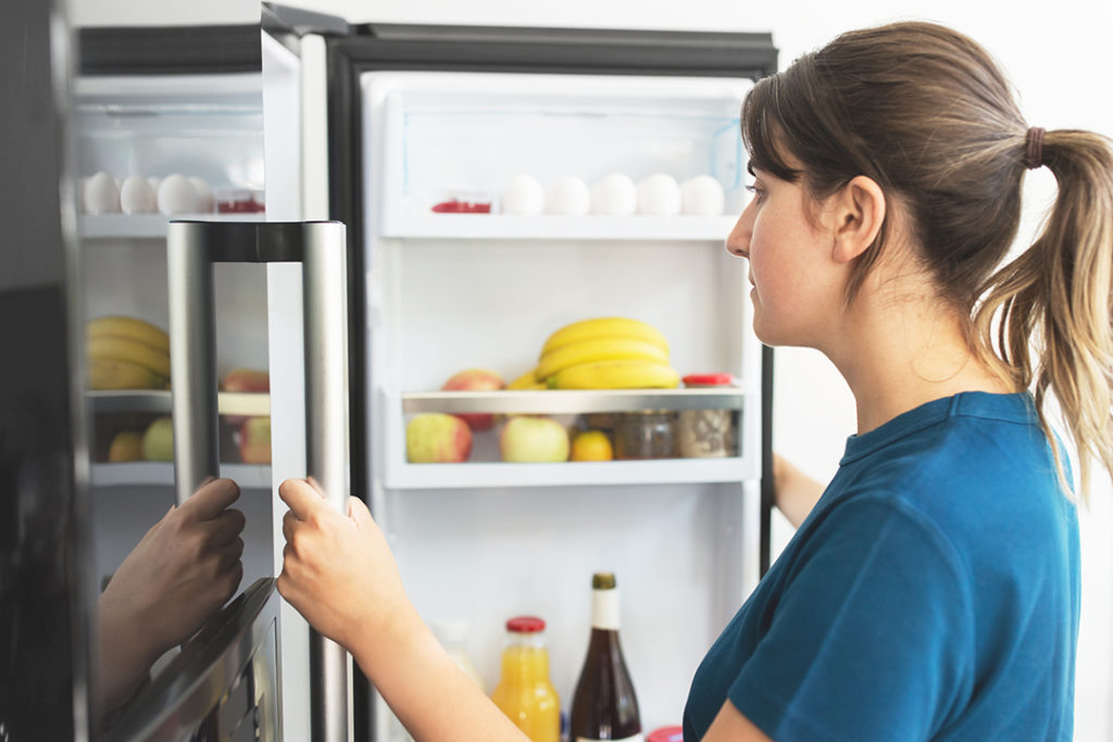 woman at open fridge at home kitchen
