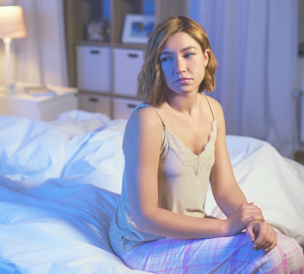 Unhappy woman in pajamas sitting on bed at night