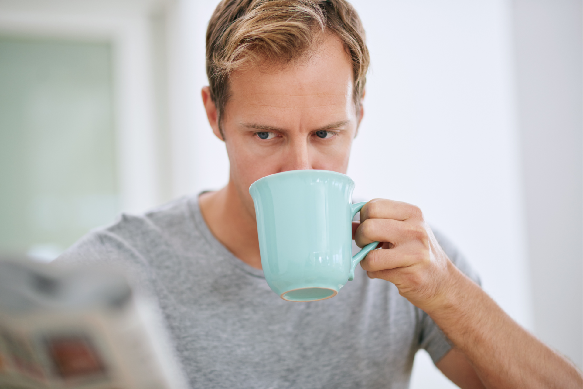 A man drinking coffee while reading the newspaper.
