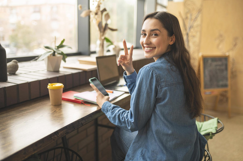 smiley woman posing with smartphone cafe while waiting her friendf