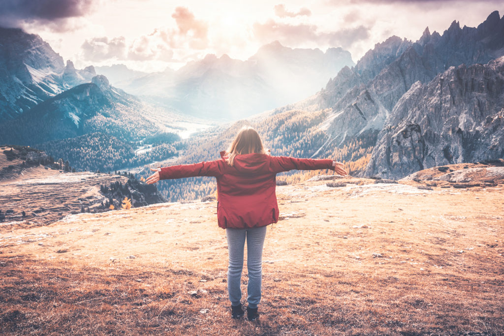 Young woman with raised up arms and mountains at sunset