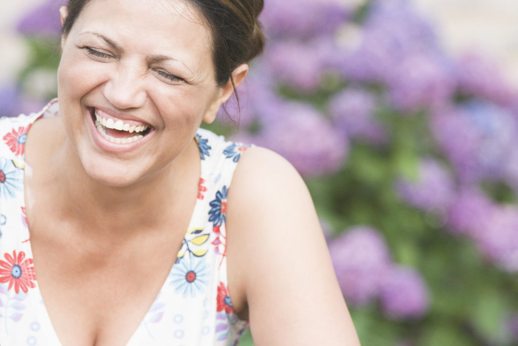 A woman laughing against a floral backdrop