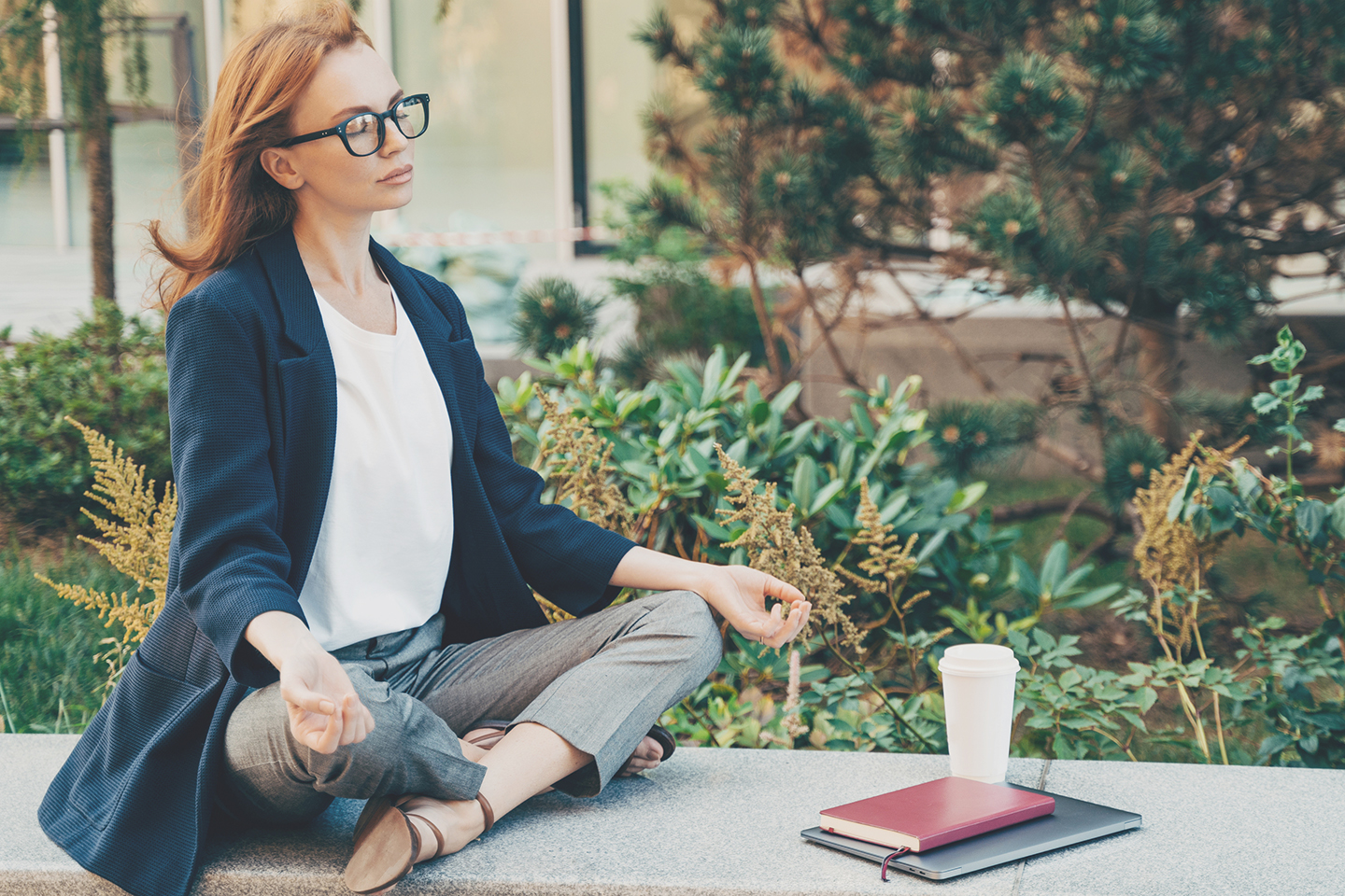 Calm red-haired woman relaxing meditating while working remotely on laptop outdoors