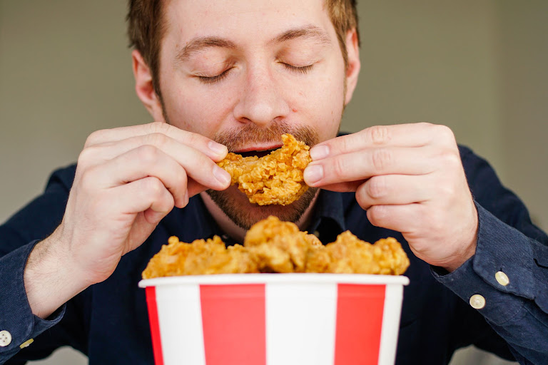 A young man eating a bucket of fried chicken.