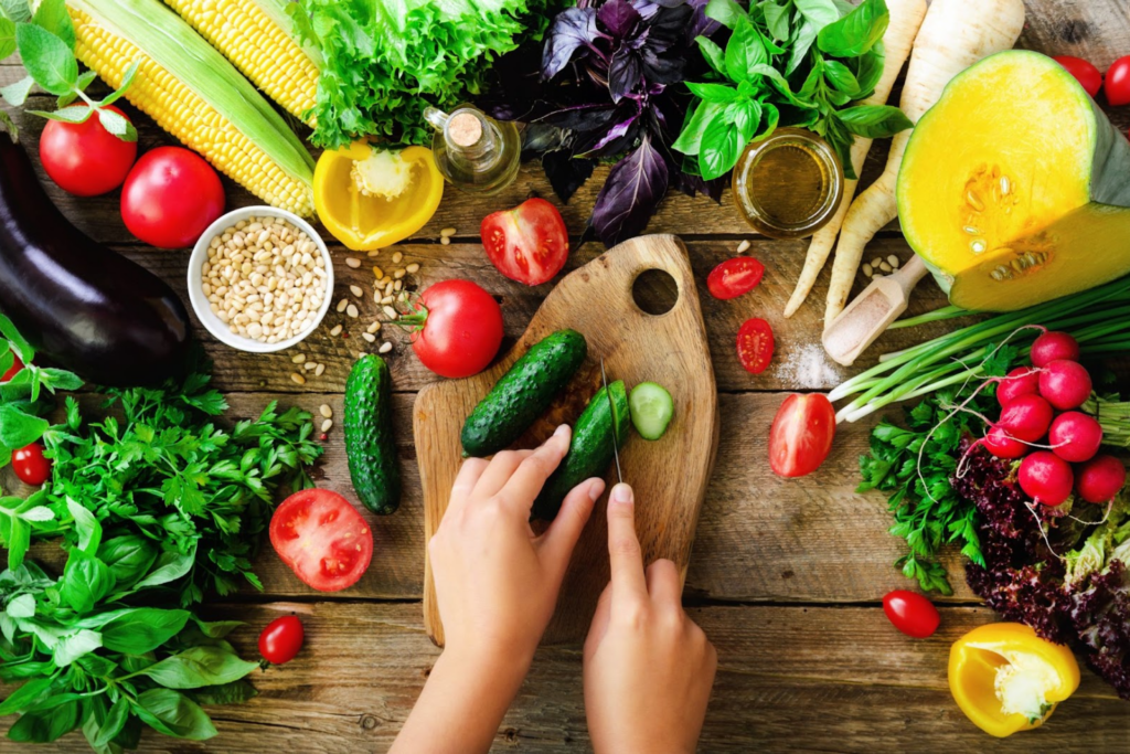 A person's hands cutting a cucumber surrounded by colorful produce.